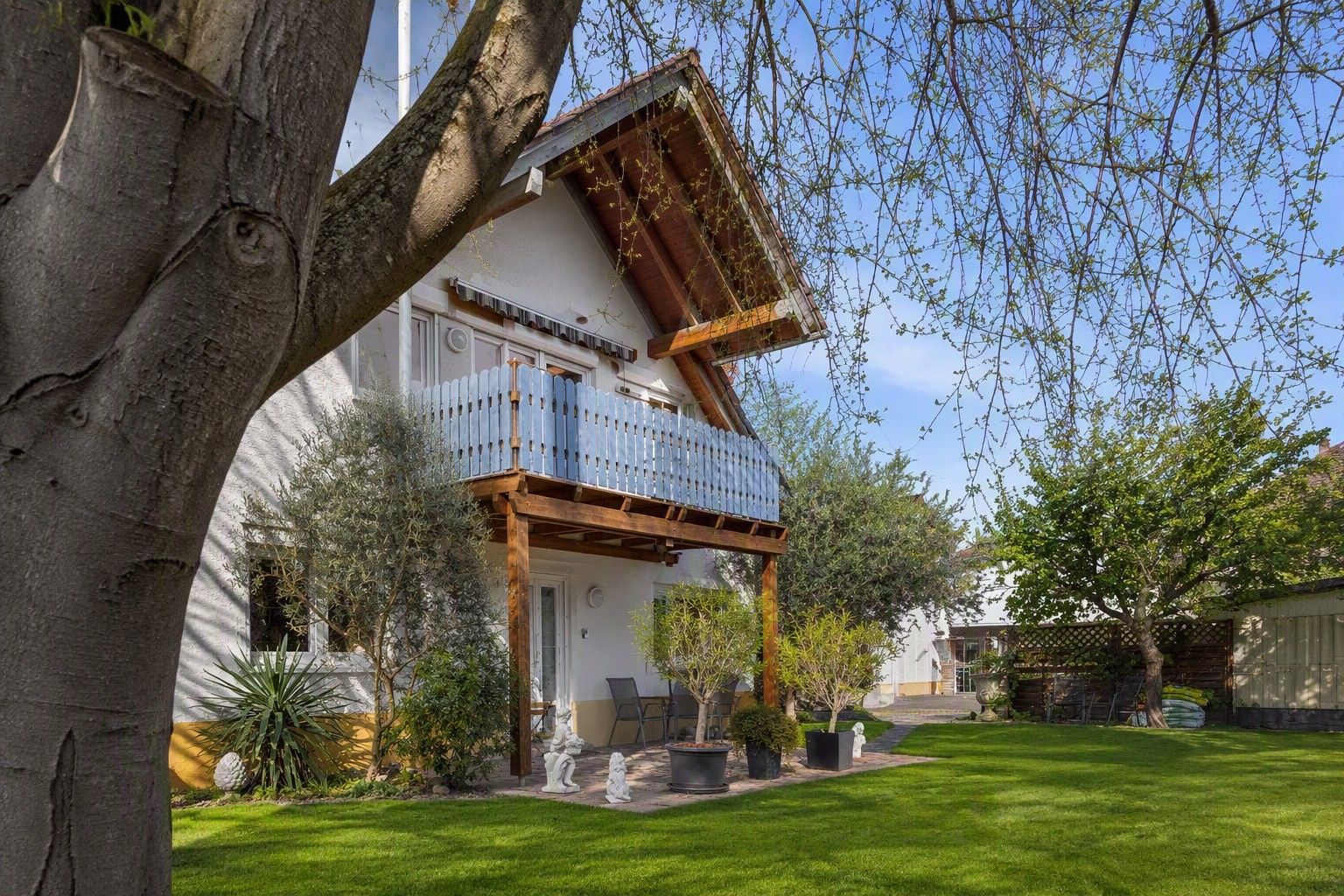 Ein zweistöckiges Haus mit Balkon, umgeben von einem gepflegten Rasen und verschiedenen Pflanzen.