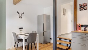 Cozinha moderna com frigorífico de aço inoxidável, soalho de madeira, mesa de jantar com cadeiras e bancada com máquina de café.