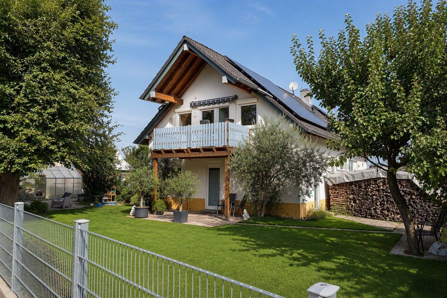 Ein zweistöckiges Haus mit Balkon, eingezäunter Hof und Gewächshaus.