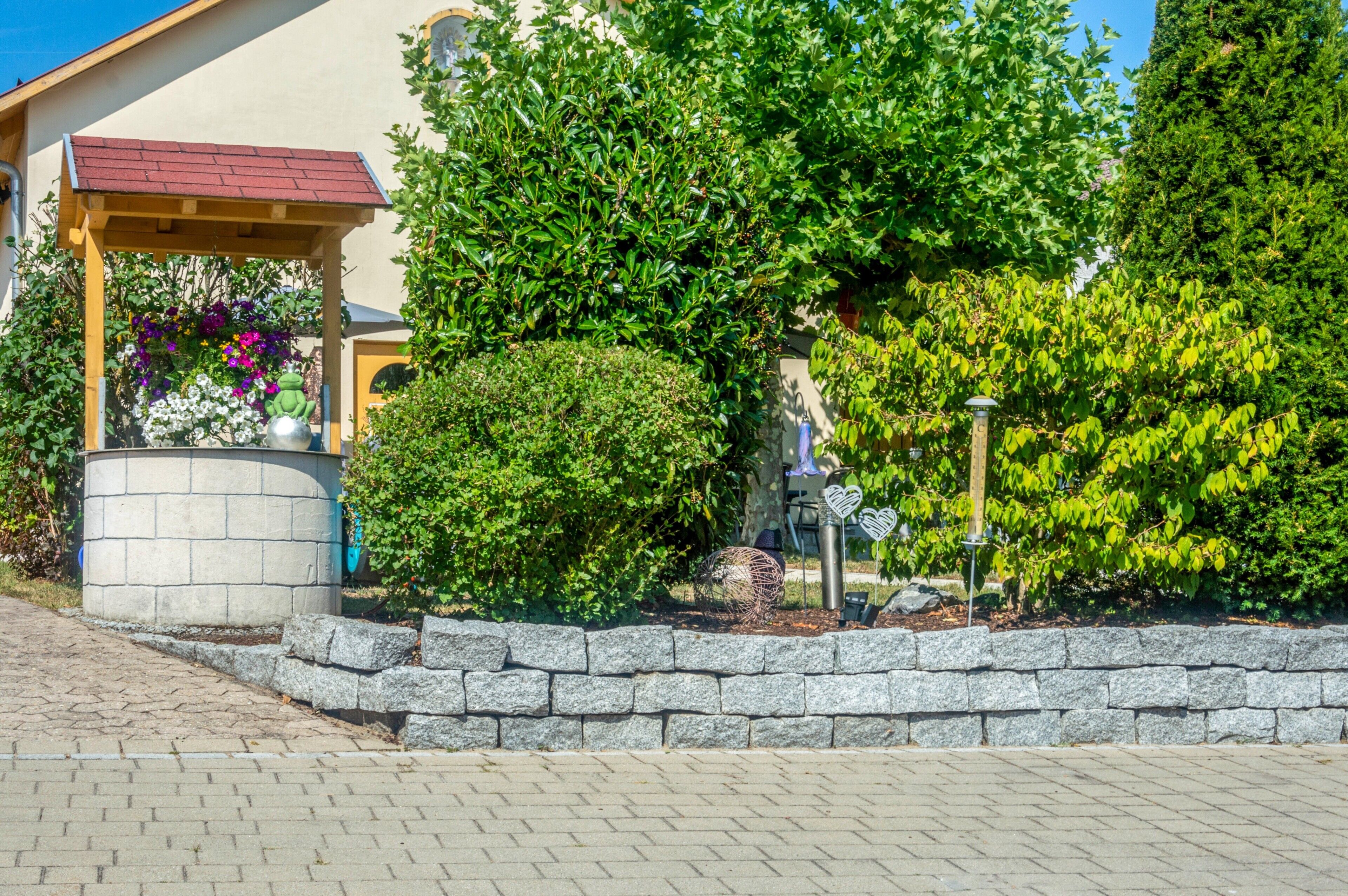 A garden area with a stone wall, a gazebo, and various plants.
