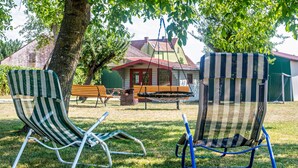 Two striped lawn chairs and a hammock in a grassy outdoor area with a building in the background.