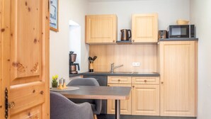 A compact kitchen with wooden cabinets, a built-in microwave, a coffee machine, and a dining area with a table and chairs.