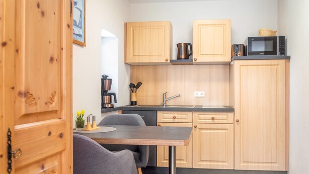A compact kitchen with wooden cabinets, a built-in microwave, a coffee machine, and a dining area with a table and chairs. - Apartment 'Hopfengarten 4' with Shared Terrace, Shared Garden and Wi-Fi (Spalt)