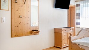 A bedroom with a wooden wardrobe, a bed, a television mounted on the wall, and a window with curtains.