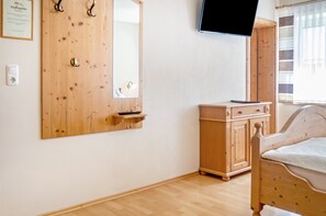 Ein Schlafzimmer mit einem Holzschrank, einem Bett, einem an der Wand montierten Fernseher und einem Fenster mit Vorhängen.