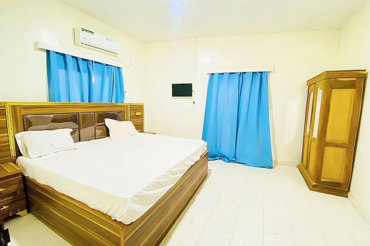 A bedroom with a wooden bed, a nightstand, a wardrobe, and an air conditioning unit.