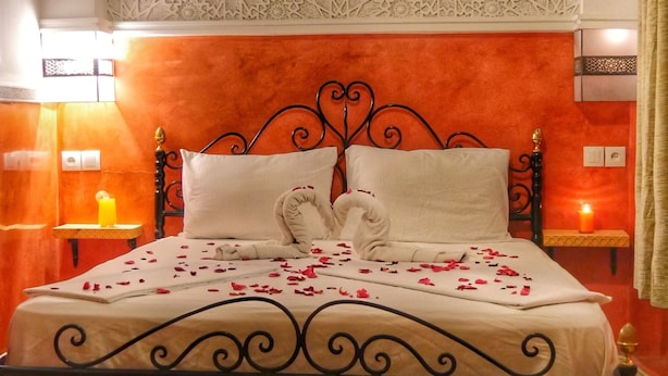 A bed with a decorative headboard, a bedside table with a candle, and a colorful rug. - Riad Seven Doors  (Marrakech)