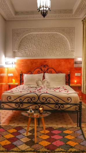 A bed with a decorative headboard, a bedside table with a candle, and a colorful rug. - Riad Seven Doors (Marrakech)