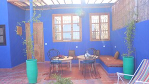 A blue-walled room with a wooden door, two windows with metal grilles, a round table with chairs, a bench, and a potted plant. - Riad Seven Doors  (Marrakech)