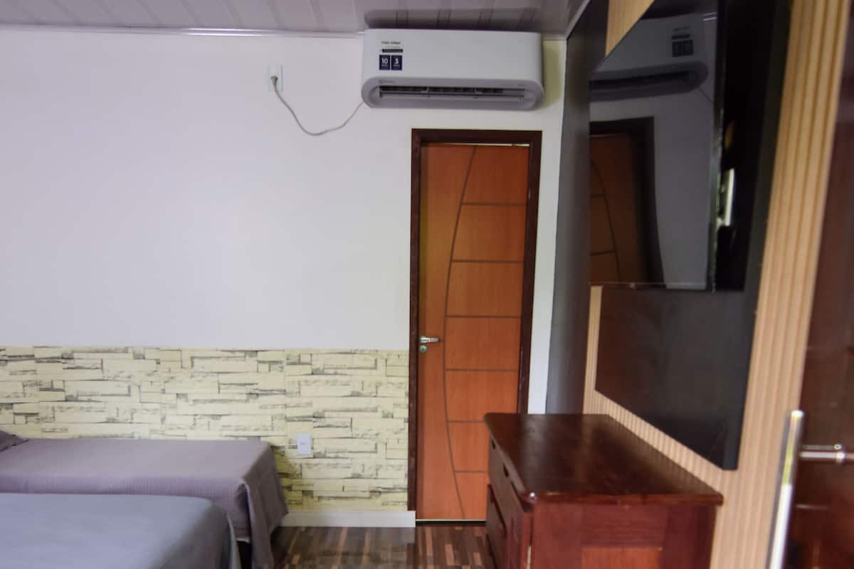 Una habitación de hotel con una cama, un aparador de madera, un televisor y un equipo de aire acondicionado.