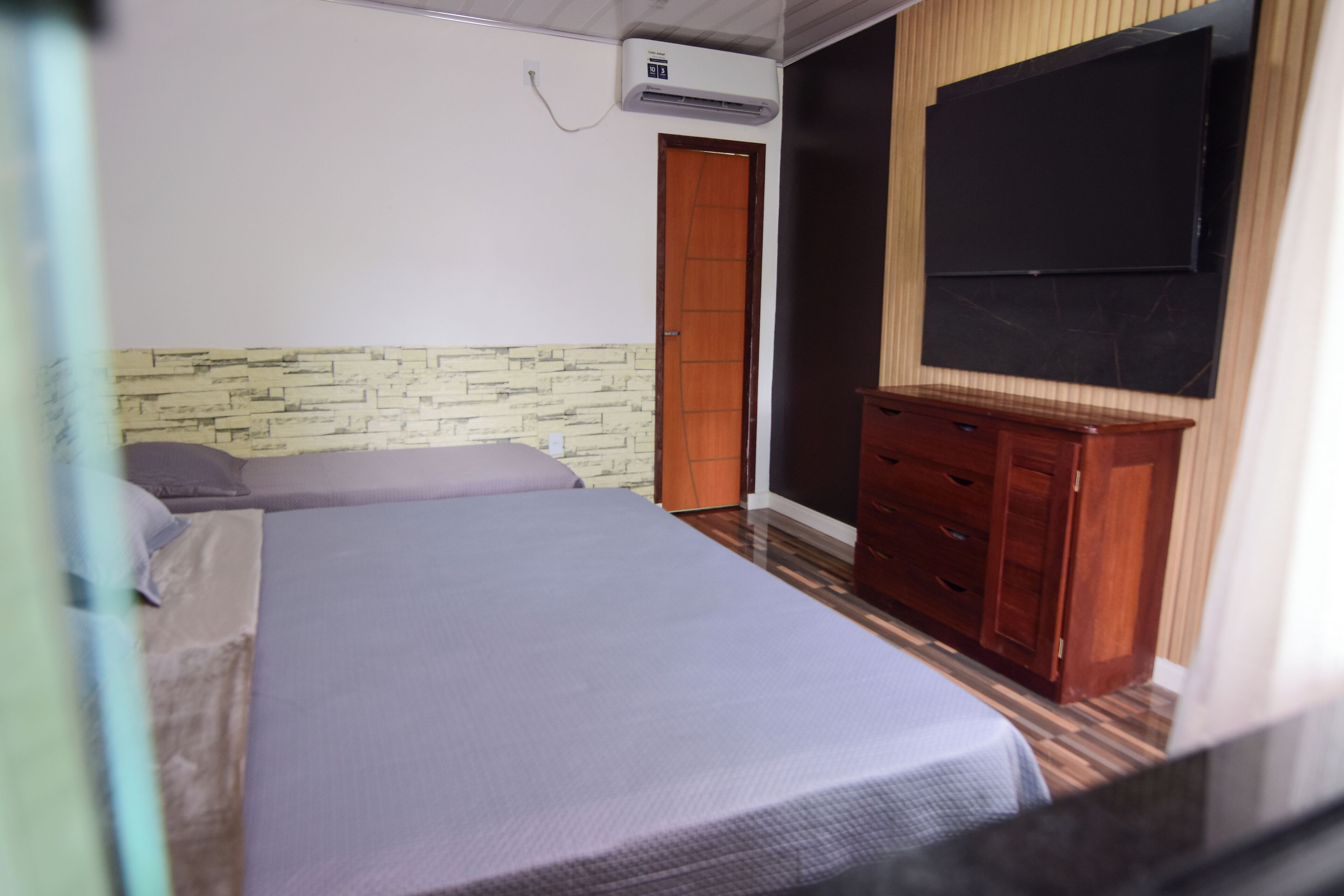 A bedroom with a bed, a dresser, a television, and an air conditioning unit.