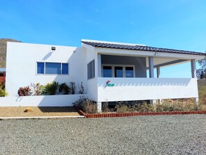 Una casa moderna de dos pisos con un porche cubierto, un pequeño jardín y un cielo azul despejado.