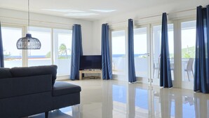 A modern living room with a sofa, a television, and large windows with curtains. - Villa Aloë - Ocean view villa with pool in Lagun (Lagun)