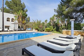 A swimming pool with lounge chairs, surrounded by palm trees and a stone wall.