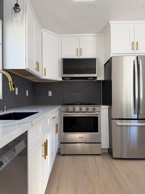 Eine moderne Küche mit weißen Schränken, einem Edelstahl-Kühlschrank, einem Einbauofen und einer Spritzschutzwand.
