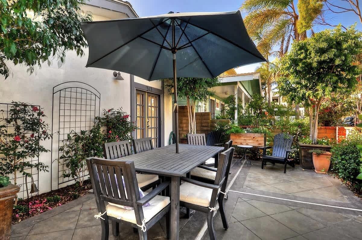 Une terrasse avec une table et des chaises, un parasol et des plantes en pot.