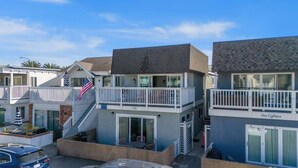 A row of two-story beach houses with balconies, numbered 120 and 121, featuring a small outdoor seating area and a flag. - Spacious Duplex with Patio and Deck, Steps to Newport Beach (Newport Beach)