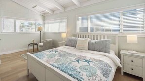 A bedroom with a bed, bedside tables, a chair, and large windows with blinds. - Spacious Duplex with Patio and Deck, Steps to Newport Beach (Newport Beach)