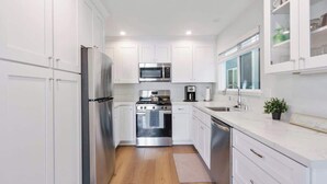 A modern kitchen with white cabinets, stainless steel appliances, and a wooden floor. - Spacious Duplex with Patio and Deck, Steps to Newport Beach (Newport Beach)