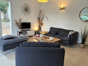 Ein modernes Wohnzimmer mit einer Couch, einem Hocker, einem Couchtisch, einem Flachbildfernseher, Wanddekoration und einer Zimmerpflanze.