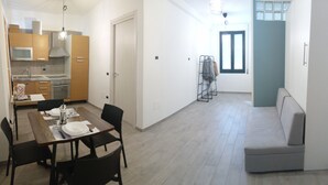 Una cocina moderna con electrodomésticos integrados, una zona de comedor con mesa y sillas de madera, un sofá gris y un tendedero.