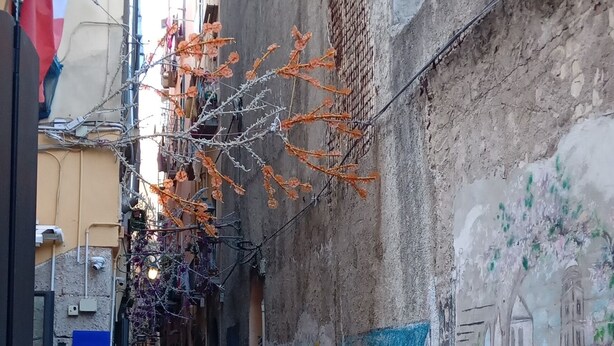Una calle estrecha con un mural, una mesa con comida y un letrero.