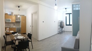 Una cocina moderna con armarios de madera, una mesa de comedor con sillas, un sofá gris y una escalera apoyada en la pared.