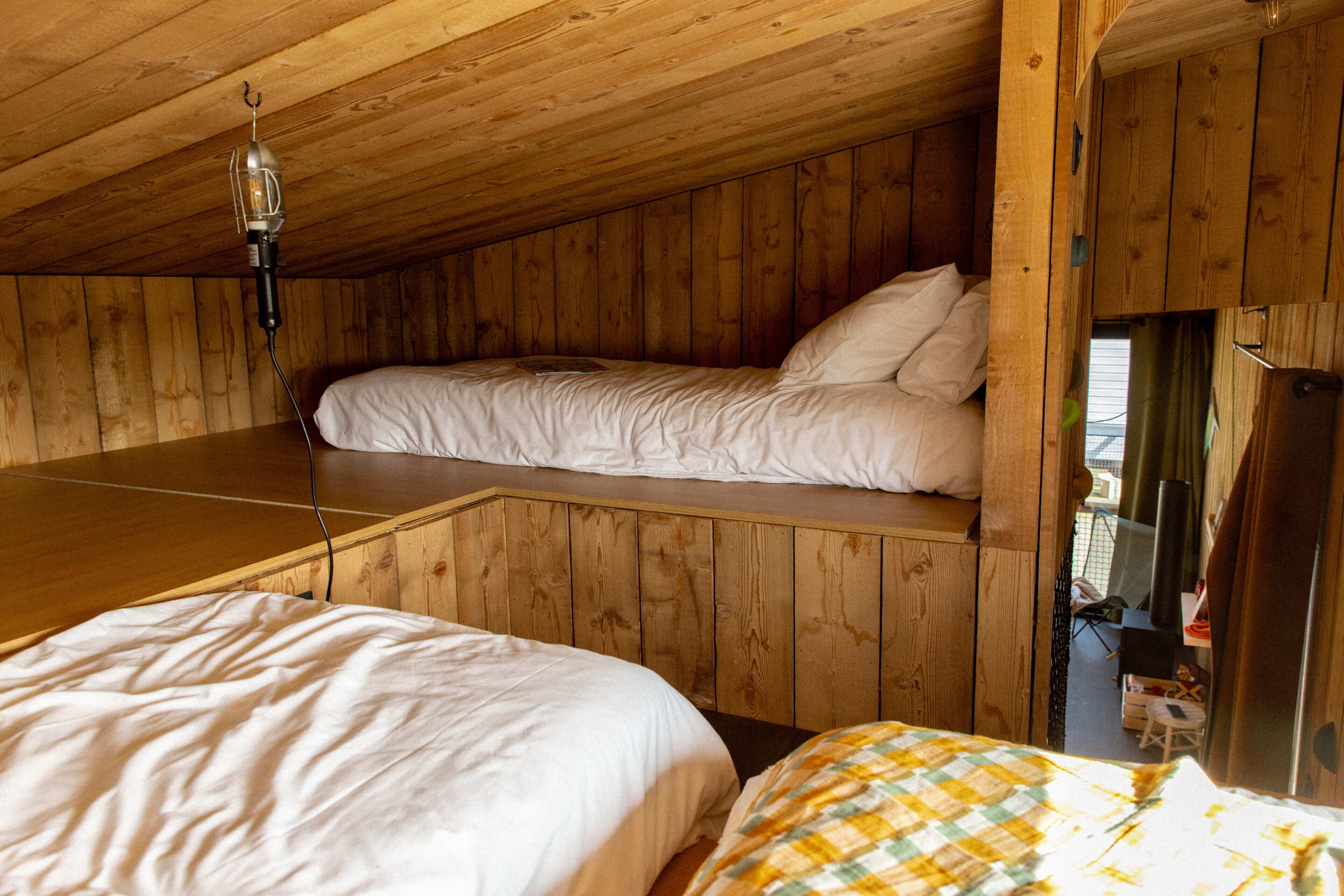 Een houten hut met twee bedden, een plafondlamp en een televisietoestel.