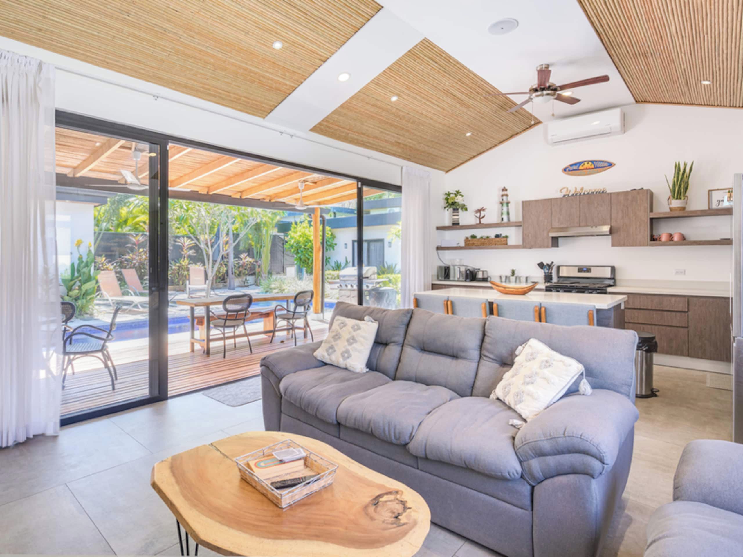 A modern living room with a grey sofa, wooden coffee table, and a view of a patio with outdoor furniture.