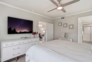 A bedroom with a bed, a dresser, a ceiling fan, a TV mounted on the wall, and a door leading to another room. - First-Floor 2 BR + Den | Bright End Unit Near Downtown Naples (Naples)