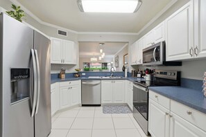 A modern kitchen with white cabinets, stainless steel appliances, and a blue countertop. - First-Floor 2 BR + Den | Bright End Unit Near Downtown Naples (Naples)