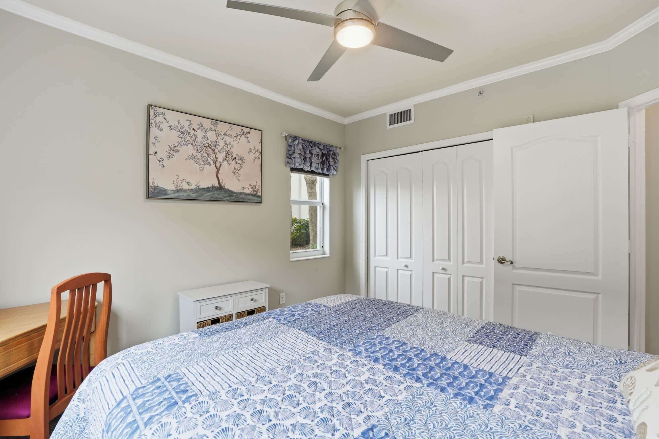 A bedroom with a bed, a ceiling fan, a window with curtains, a door, and a small dresser.