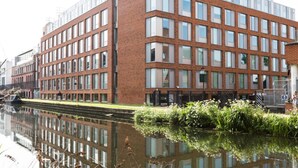 Een modern gebouw met een bakstenen gevel en grote ramen, gelegen naast een gracht.
