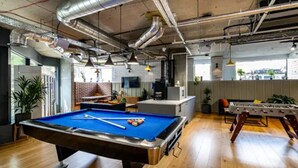 Een pooltafel in een ruimte met zichtbare ventilatiekanalen, een tafelvoetbalspel en een bar.