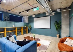 A conference room with a large screen, seating, and a clock on the wall. - Student Only Modern Studio at Portobello Near Kensington and Chelsea (London)