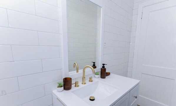 A bathroom with white tiled walls, a white sink with gold faucets, and a mirror above the sink.