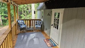 A covered porch with a wooden railing, a blue mat at the entrance, and a door to a building. - The Cozy Cove Cabin, in Townville, on Lake Hartwell. (Townville)