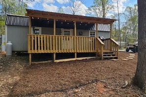 A wooden deck with a covered area, a water tank, and a vehicle in the background.