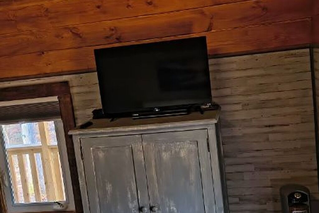 Un interior de madera con una televisión de pantalla plana montada en un mueble, una ventana con persianas y una puerta.