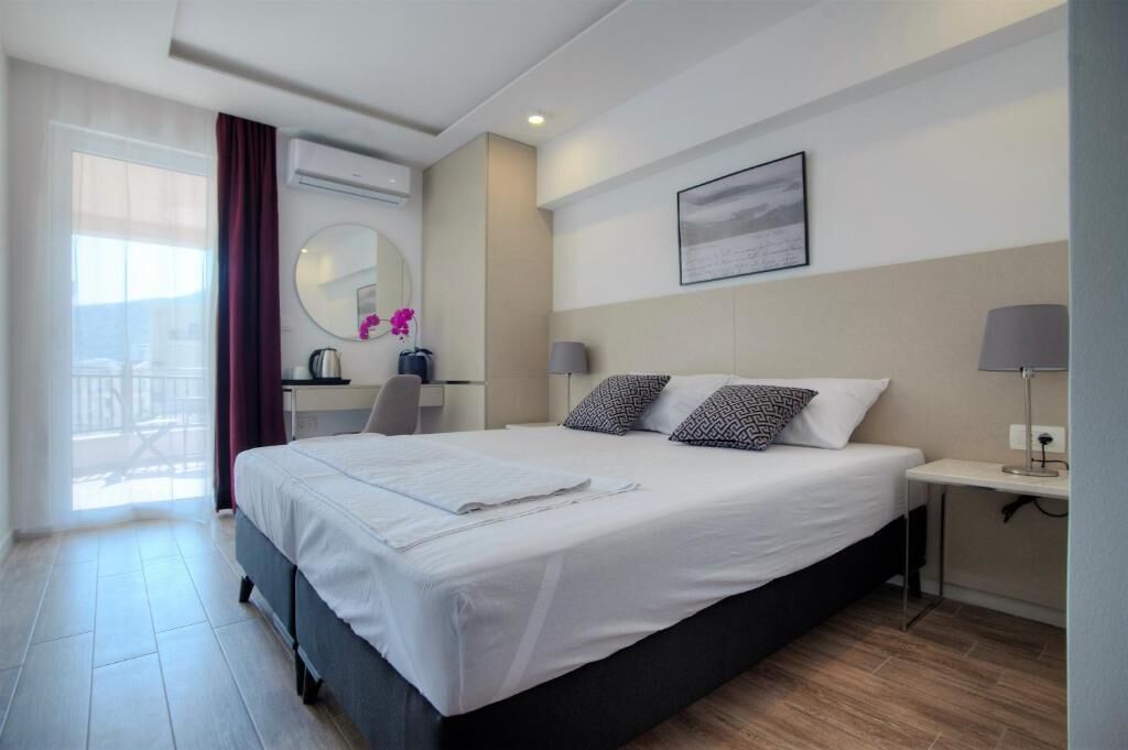 A hotel room with a bed, a desk, a chair, a lamp, a mirror, and a window with curtains.