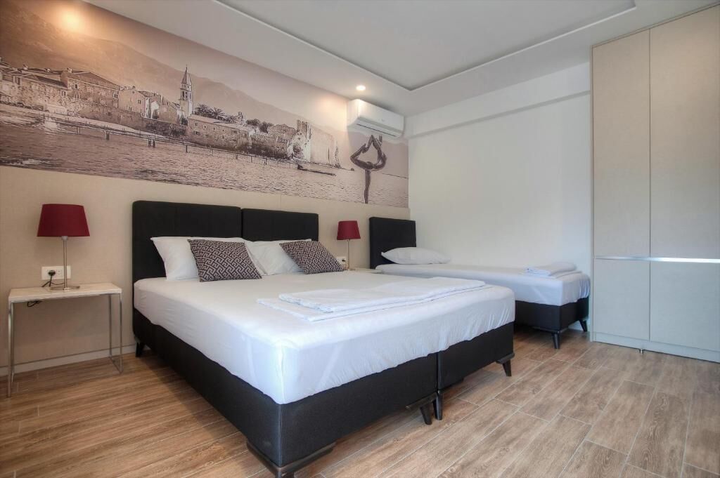 Una habitación de hotel con una cama grande, una cama más pequeña, una mesita de noche con lámpara y un armario.