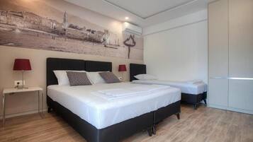 Una habitación de hotel con una cama grande, una cama más pequeña, una mesita de noche con lámpara y un armario.