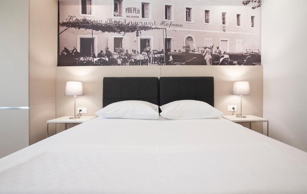 Habitación de hotel con una cama, dos mesitas de noche, dos lámparas y un cartel grande en la pared.