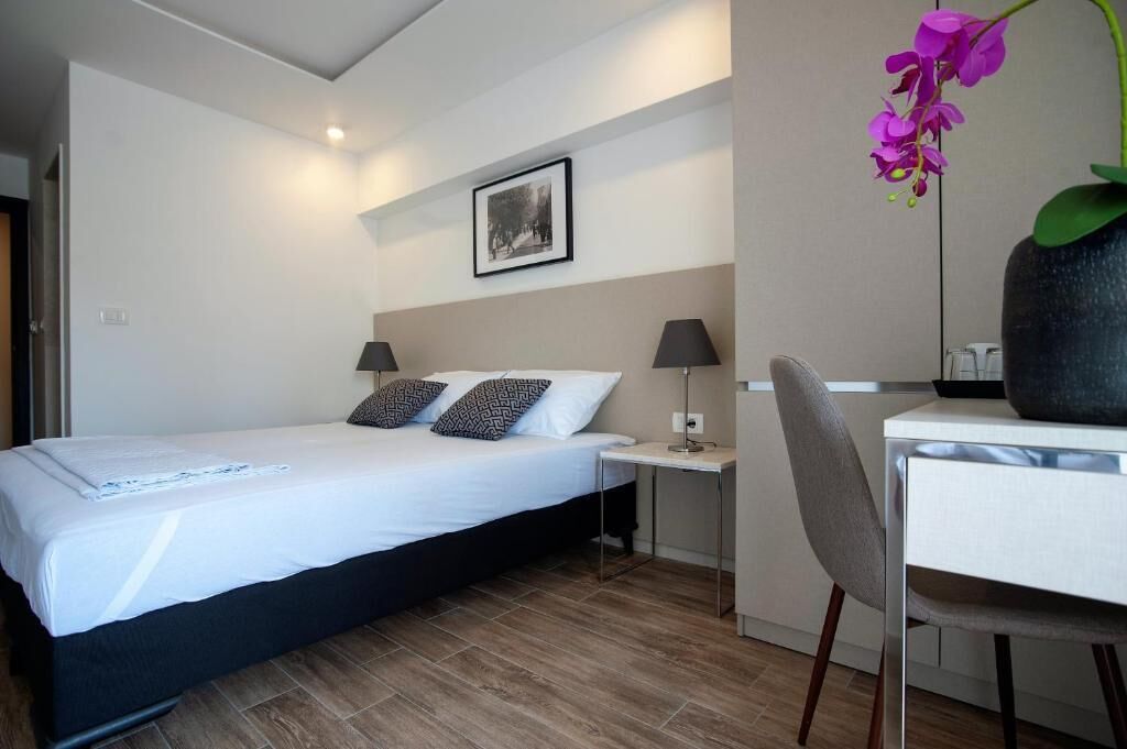 Habitación de hotel con cama, mesitas de noche, escritorio, silla, un cuadro en la pared y una orquídea en maceta.