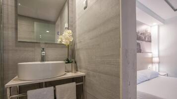 A modern bathroom with a large mirror, a sink, and a vase of white flowers.