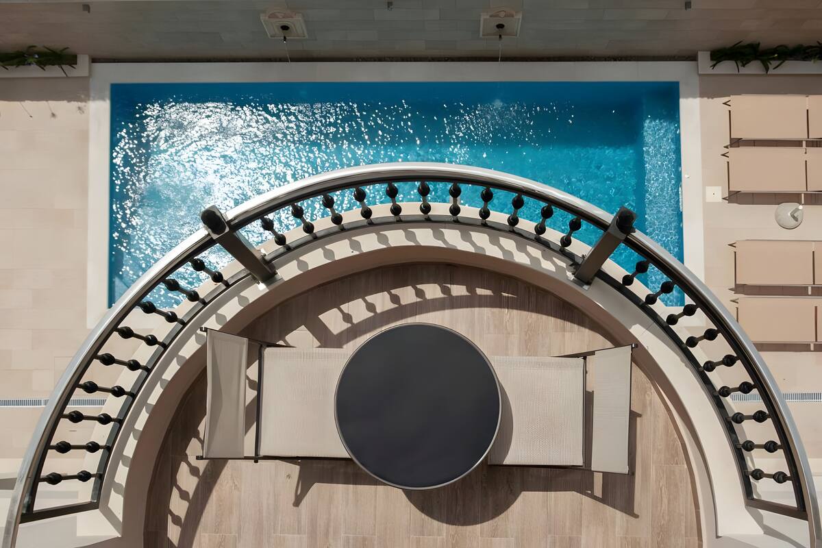 Ein Pool mit glatter, blauer Wasseroberfläche, einer runden Sitzgruppe in der Mitte und einer gebogenen Balkonbrüstung.