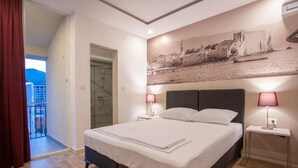 A bedroom with a bed, two bedside lamps, a glass door leading to a balcony, and a wall-mounted picture. - Casa Mia (Budva)