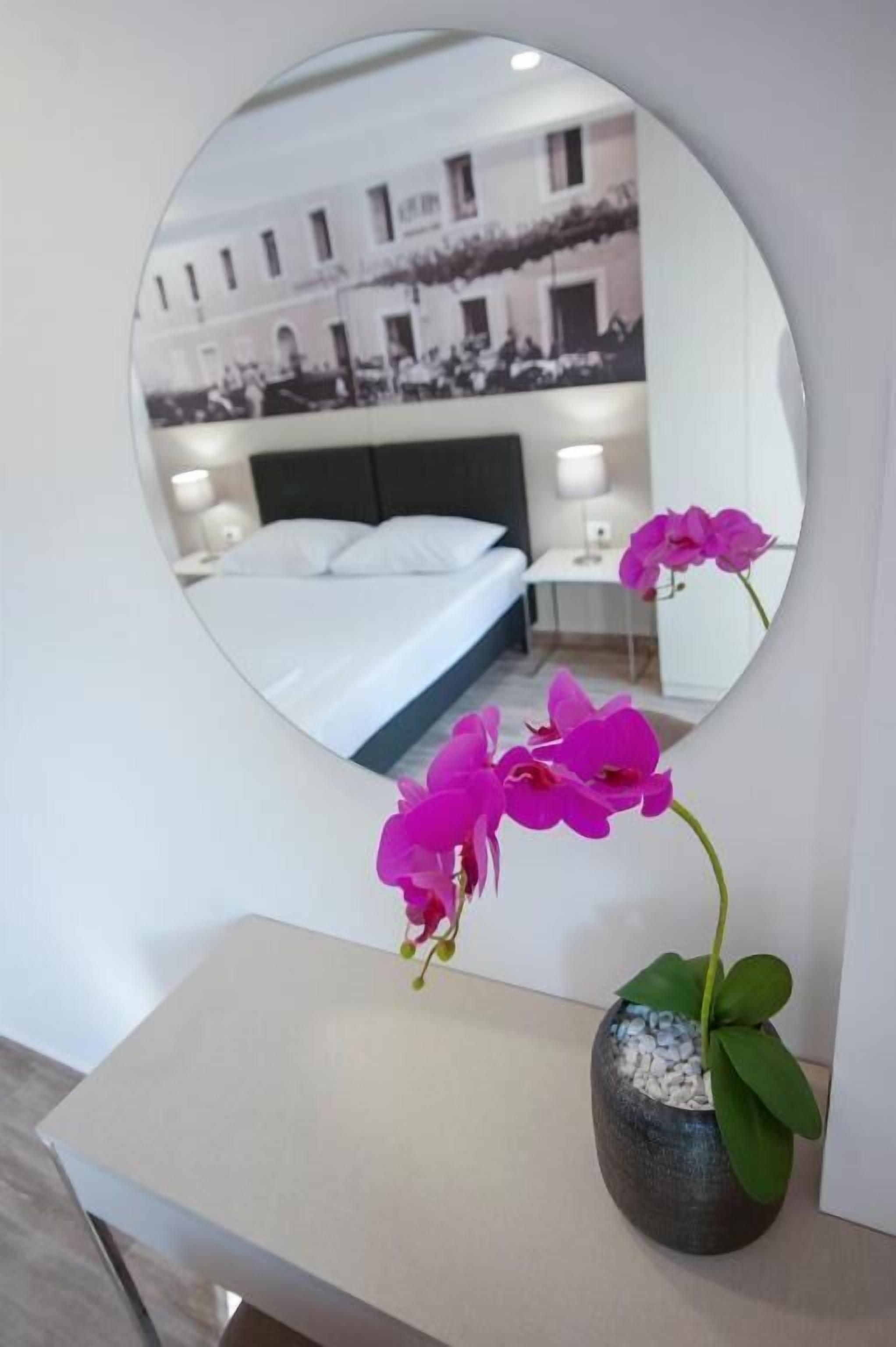 A hotel room with a bed, bedside table, and a mirror reflecting the room.