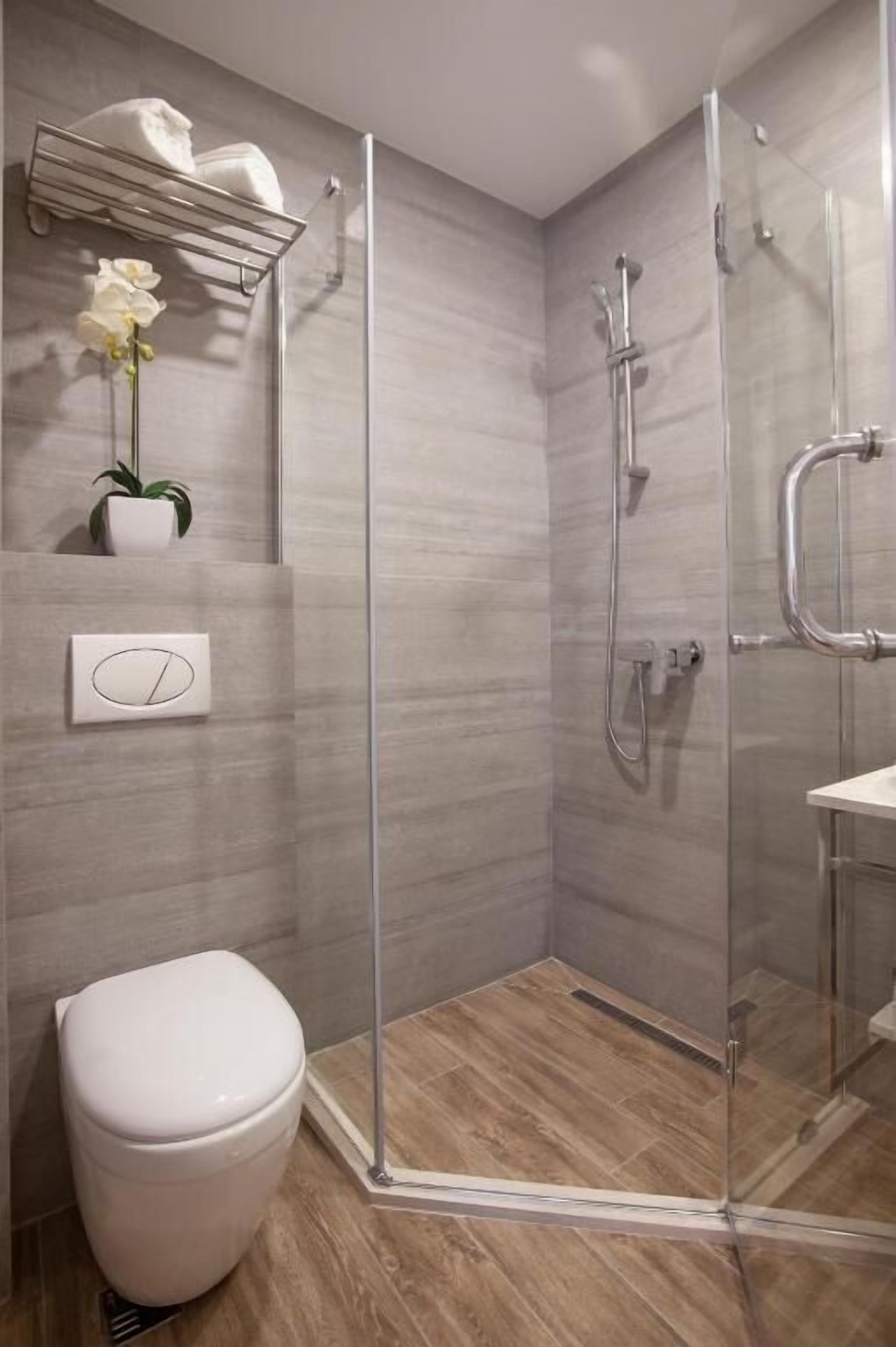 Un baño moderno con ducha de vidrio, inodoro y toallero con una planta.