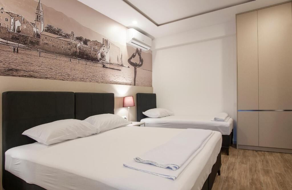 A hotel room with two beds, a wall mural, a wardrobe, and a bedside lamp.